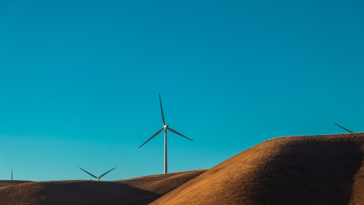 Wind turbines on sandy dunes under a clear blue sky, showcasing renewable energy in a desert environment.