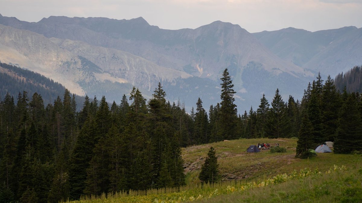 Picturesque camping scene in a forested valley surrounded by mountains.