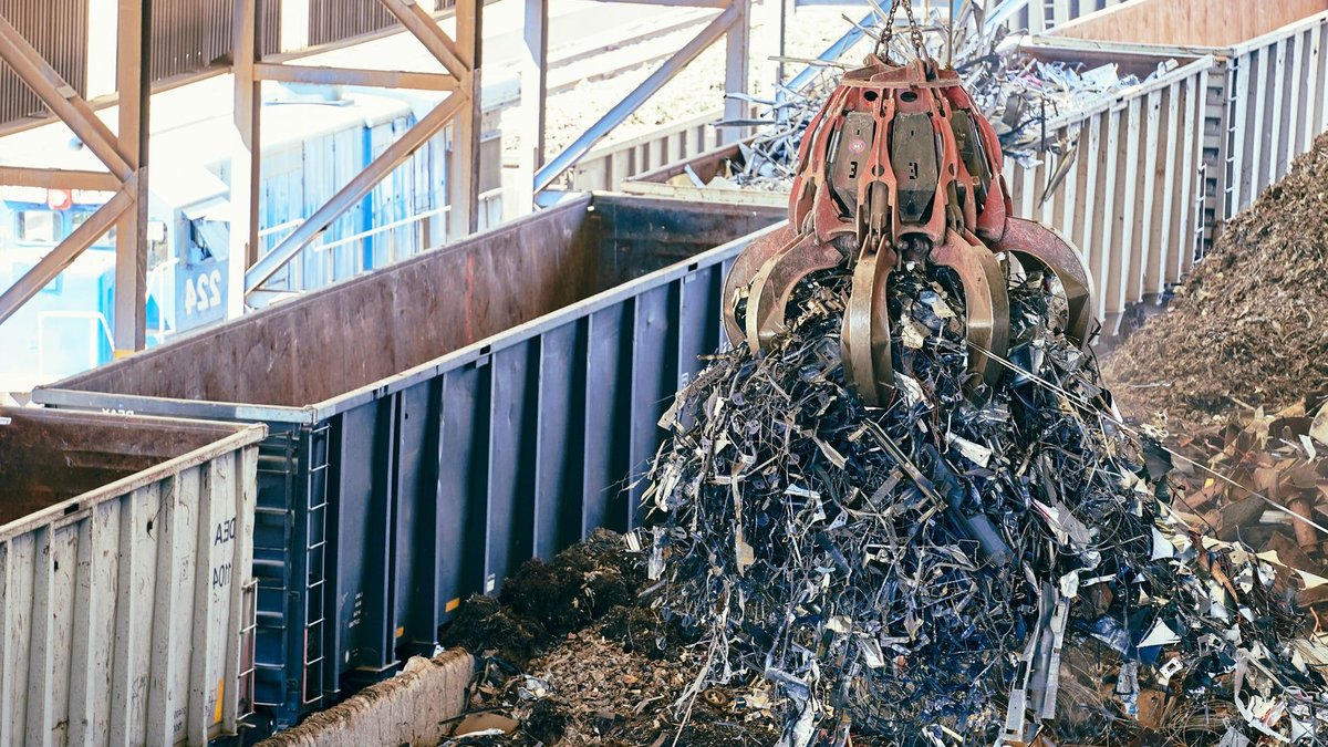 An industrial claw crane lifts metal scrap in a recycling facility, showcasing efficient waste management.