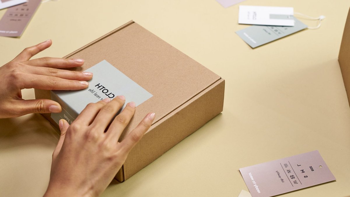 Hands carefully packing a cardboard box with multiple tags around, emphasizing sustainable packaging.