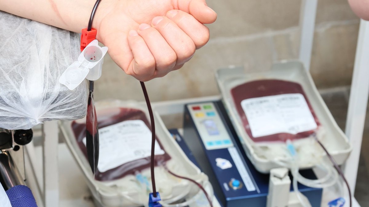 Close-up of blood donation process showing a donor's arm and blood bags in a clinic.