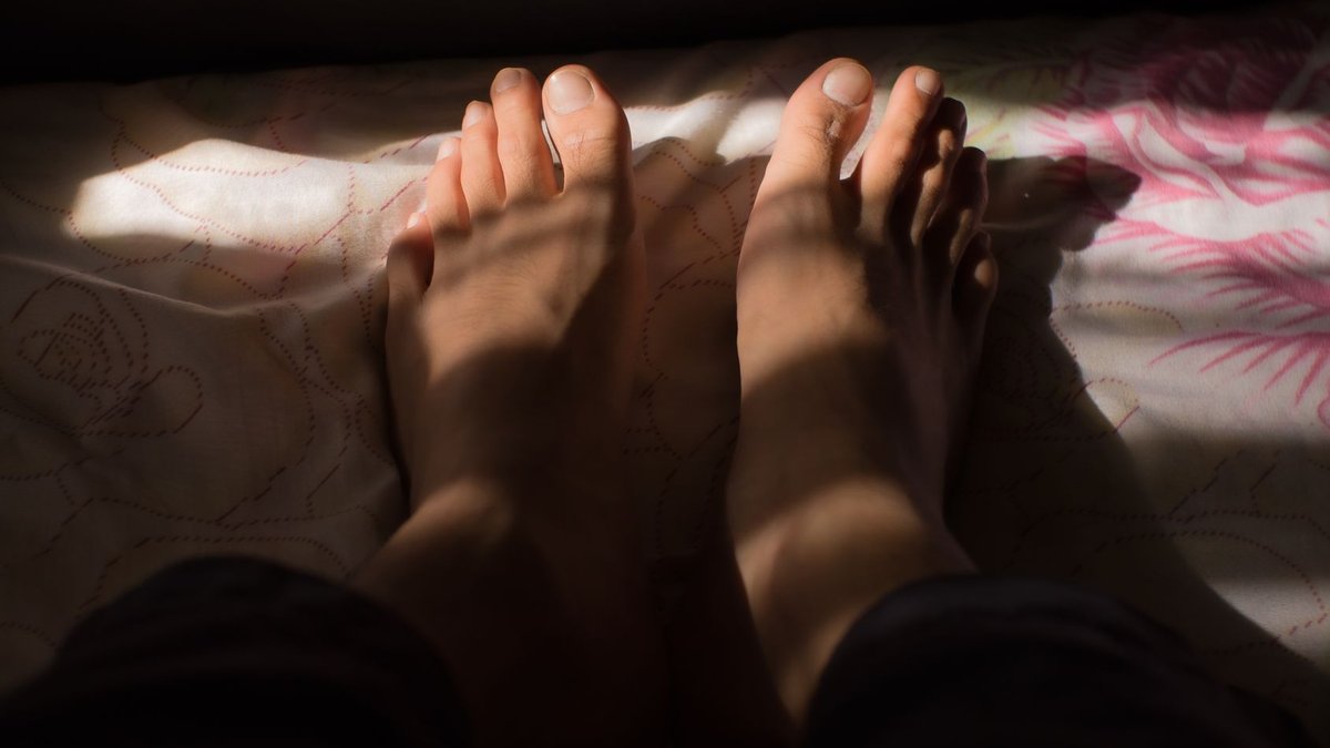 A close-up shot of bare feet casting shadows on a patterned bedspread.