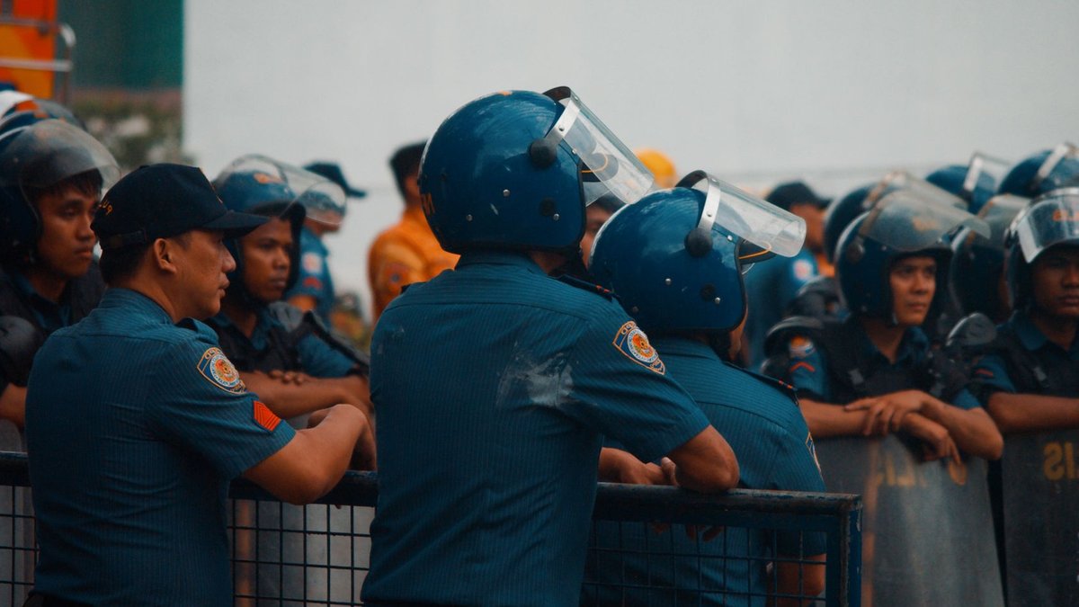 Five Charged After Ambush Frees Handcuffed Suspect Group of police officers wearing riot gear during a daytime protest outdoors.