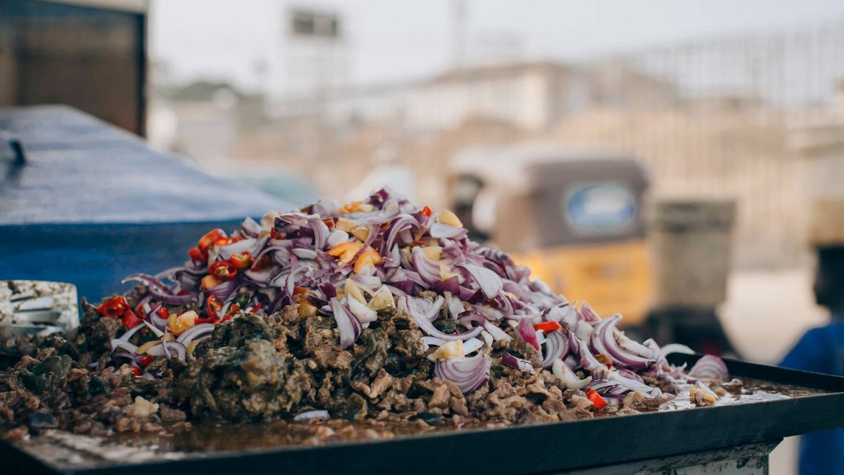 Outdoor street food stall with chopped onions and meat in a bustling city.