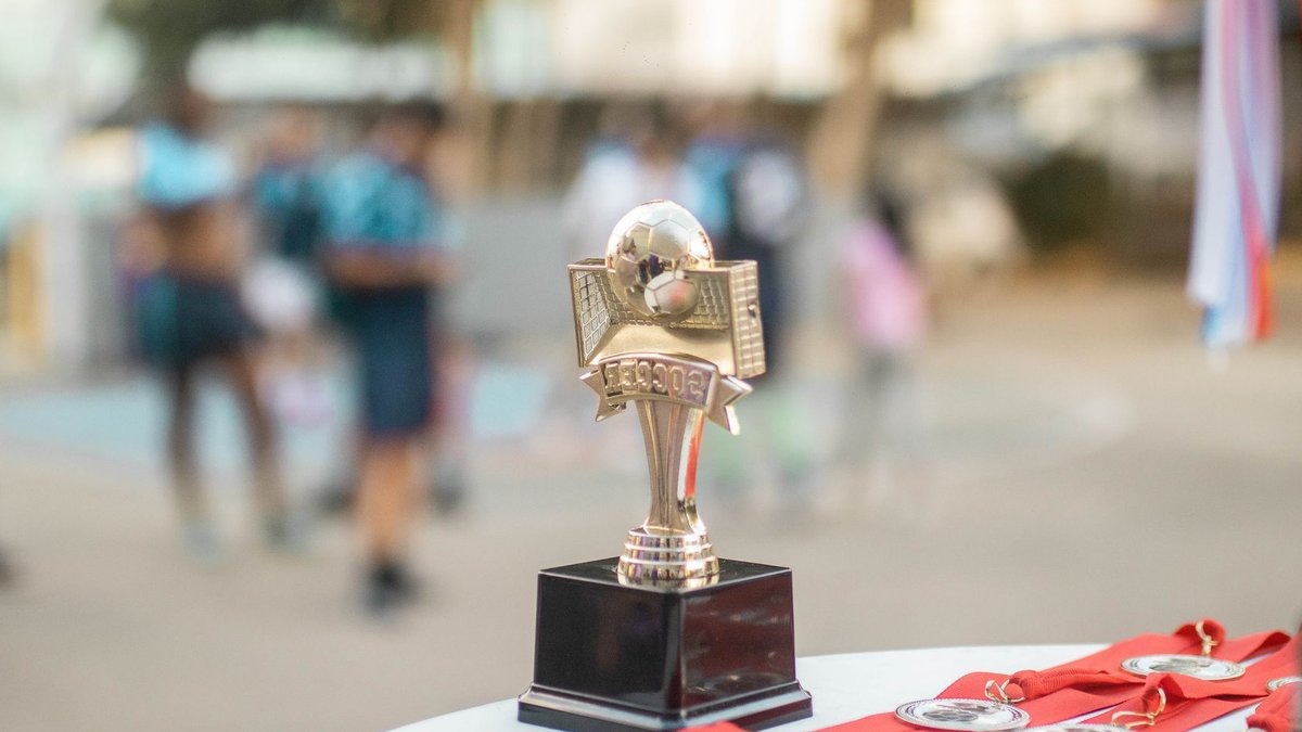 Designers invited to submit award entries now Close-up of a polished soccer trophy with medals at an outdoor sports award ceremony.