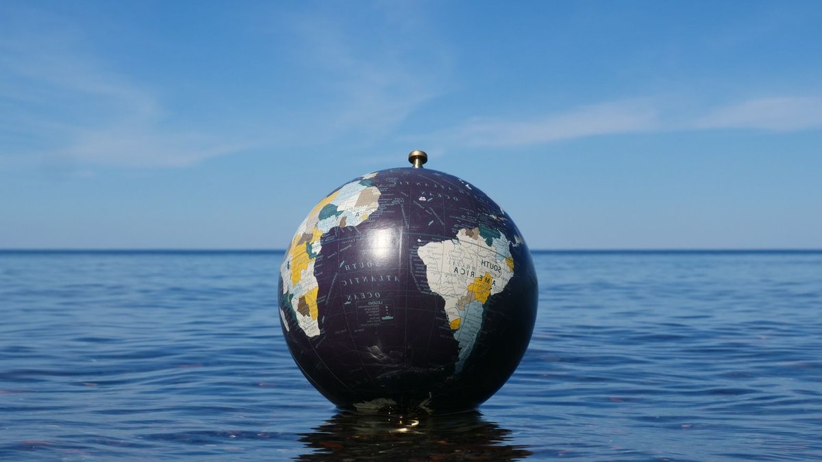 World globe floating on calm ocean water with clear blue sky background, symbolizing global environment concepts.