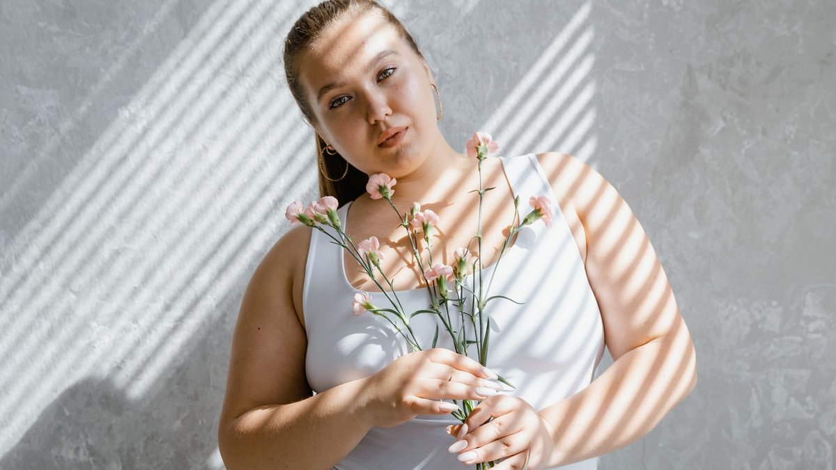 Safaricom rolls out affordable multi-branch network service Plus-size woman in tank top holding flowers with sunlight filtering through blinds.
