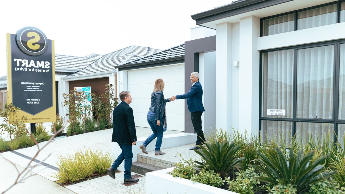 A realtor shakes hands with potential buyers outside a modern model home.