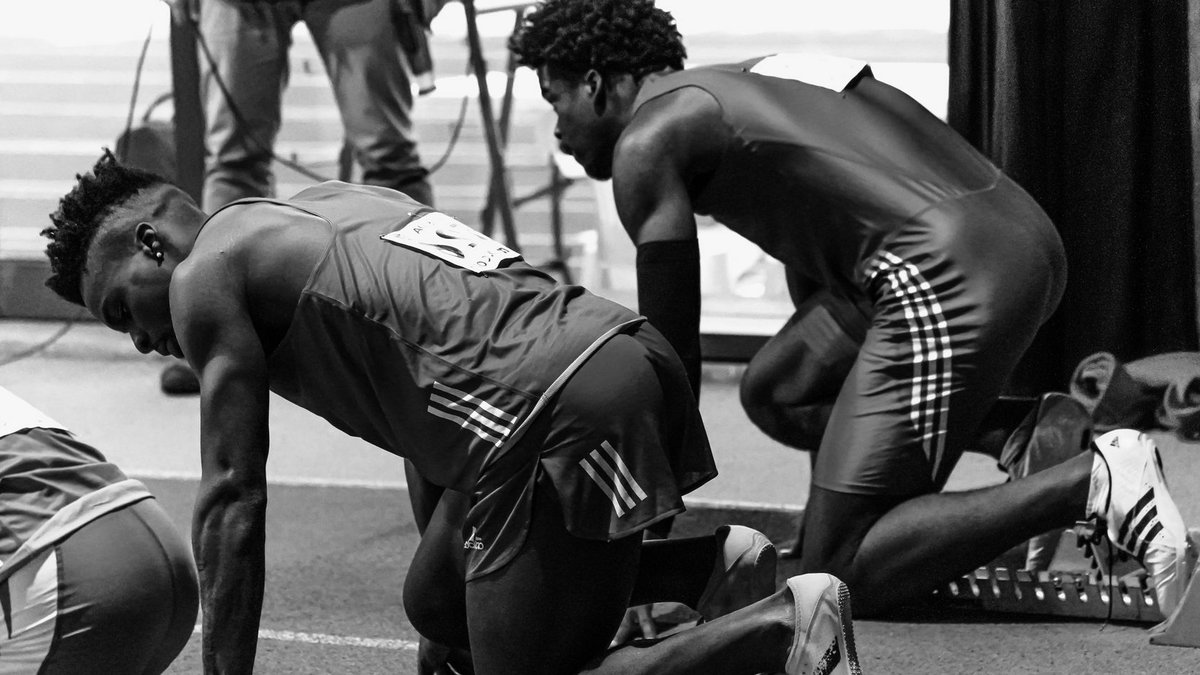 Black and white image of athletes in starting blocks ready for a sprint race indoors.