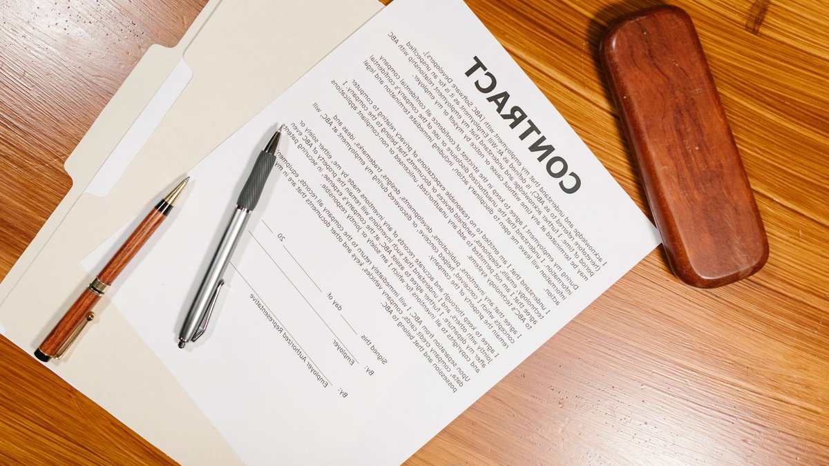 High-angle view of a contract document with pens and a case on a wooden table.