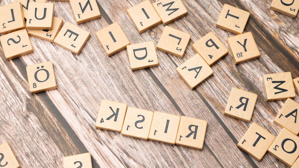 Scrabble tiles spelling out 'risk' scattered on a rustic wooden background, symbolizing uncertainty.