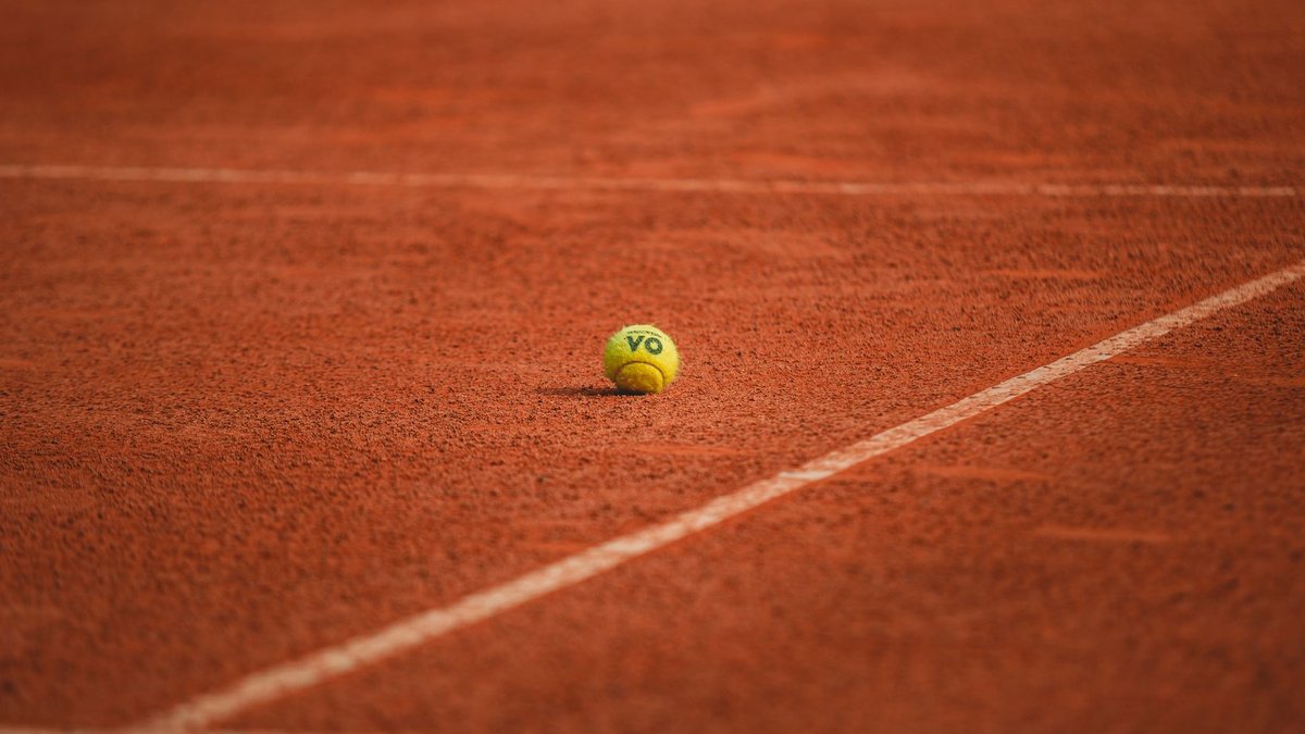 Court Approves Class-Action Suit Over Illegal Tariffs A lone tennis ball rests on a red clay tennis court, highlighting its vibrant texture.