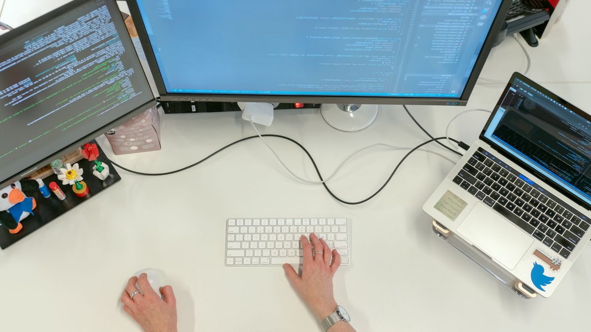 A female software engineer coding on dual monitors and a laptop in an office setting.