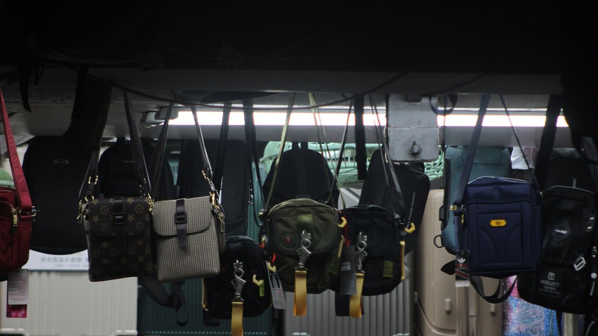 Colorful bags and luggage hang on display in a dimly lit market setting.