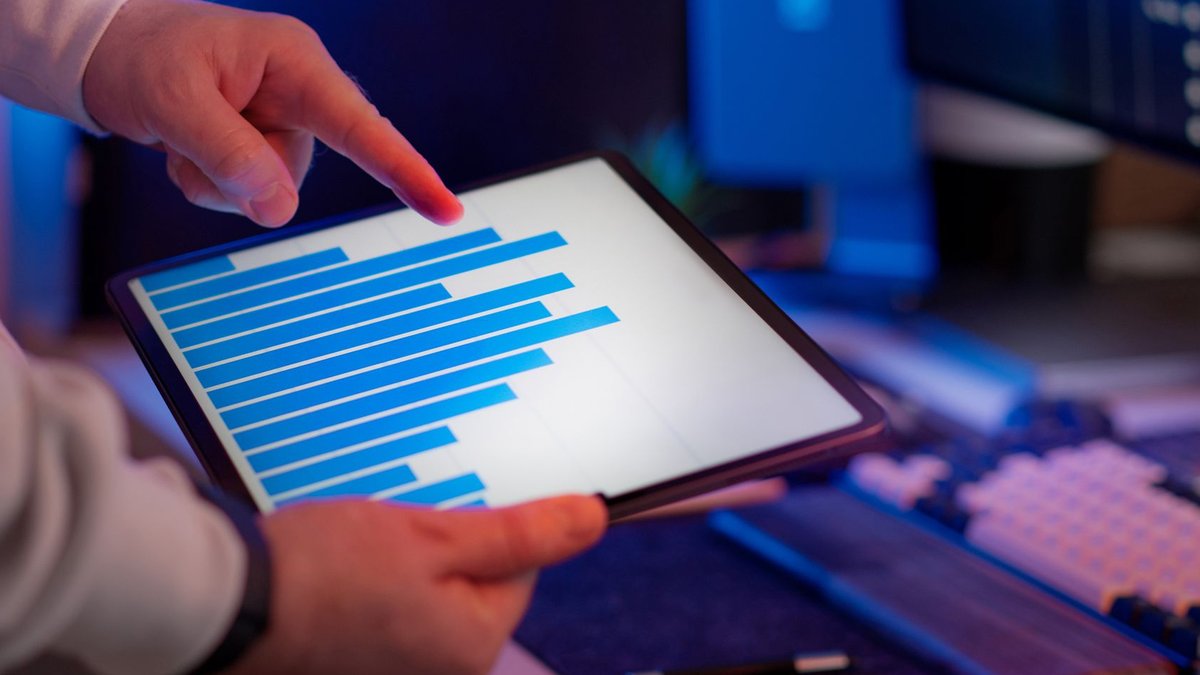 Business professional analyzing bar chart on tablet in office setting, highlighting data insights.