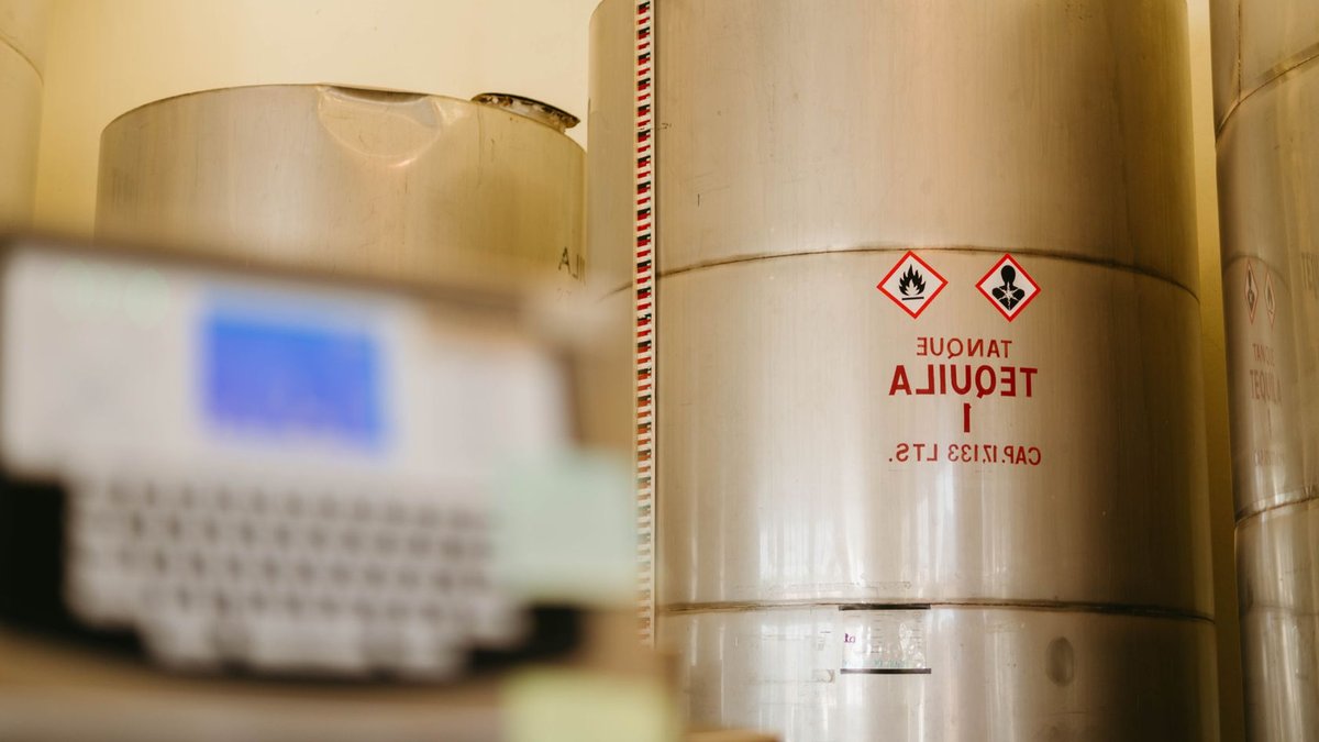 Close-up of tequila storage tanks in a distillery with safety warnings, showcasing tequila production.
