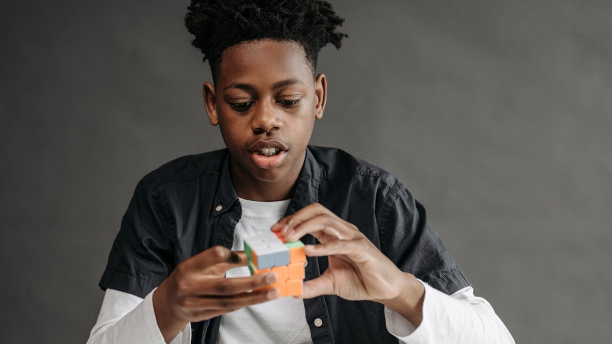 Girl shatters Rubik's Cube record twice Young black teenager solving a Rubik's Cube in a studio setting on a gray background.