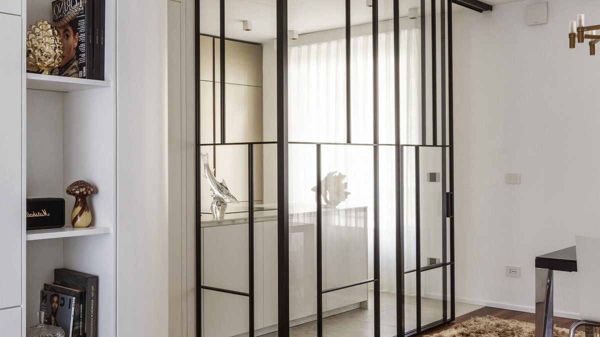 Glass-walled kitchen creates room within Turin apartment A glass-enclosed kitchen in a Turin apartment features floor-to-ceiling black metal frames, a sliding glass door, minimalist