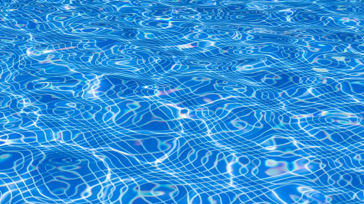 Lehigh Valley Pool Prep Focuses on Sustainability, Safety Aerial view of a sparkling, clean backyard swimming pool surrounded by lush greenery and vibrant flowers, under a bright, cle