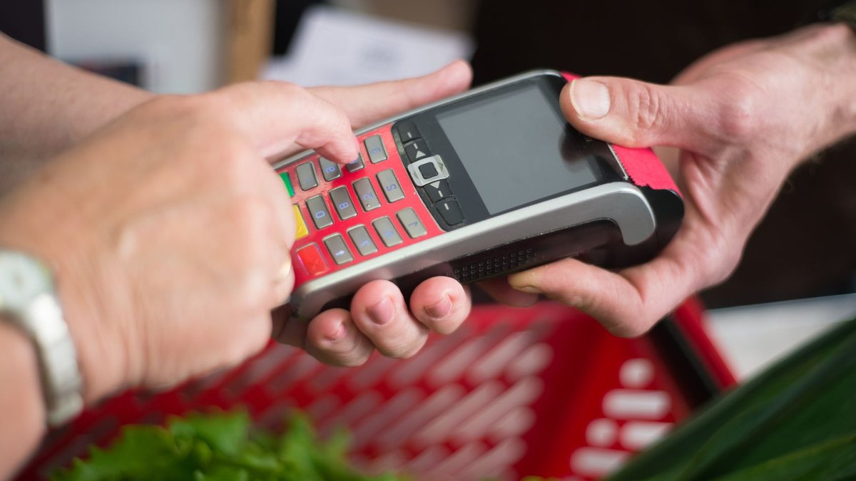 Two people making a cashless payment at a grocery store with a credit card terminal.
