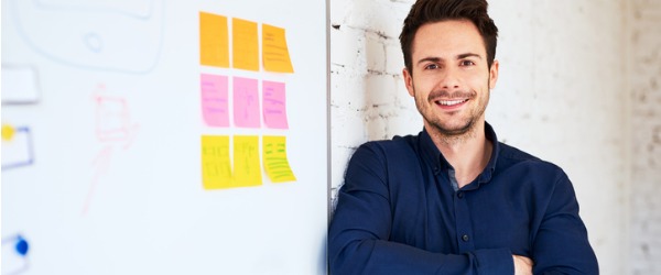 A web developer standing beside a white board, smiling for the camera.