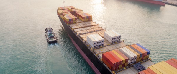 A cargo ship guided by a tug boat.