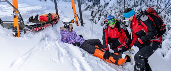 Two ski patrollers providing emergency medical care to a young girl on a mountain.