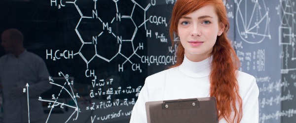 Um estudante de física em pé em frente de um quadro negro numa sala de aula.