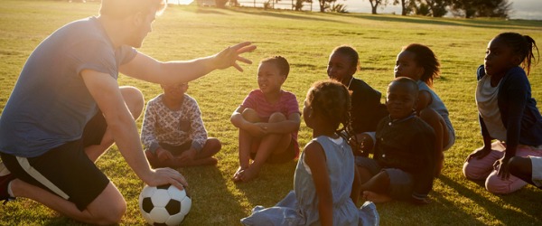 A physical education teacher on a soccer field talking to his students.