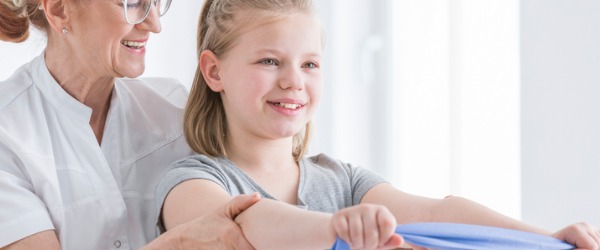 An occupational therapist helping a little girl use an exercise band.