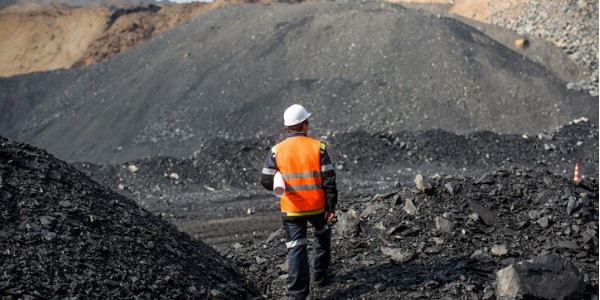 A mining and geological engineer walking through a mining site with drawings tucked under his arm.
