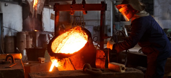 A metal caster pouring molten liquid metal into a mold.