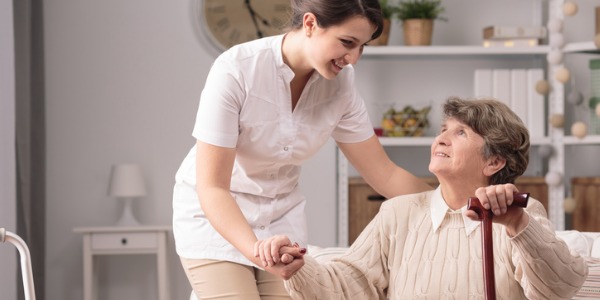 Ein häuslicher Gesundheitsberater, der einer älteren Frau hilft, mit einem Stock aufzustehen.