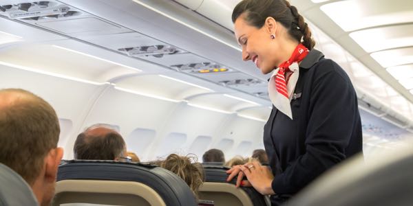 A flight attendant speaking and smiling with a passenger on a flight.