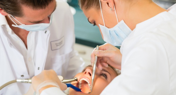 A dental assistant working alongside a dentist, using suction.