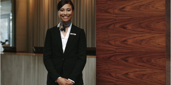 A concierge in a hotel lobby smiling and waiting to help a guest.