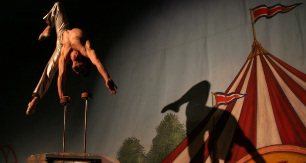 A circus performer doing a single hand stand high up in the air.