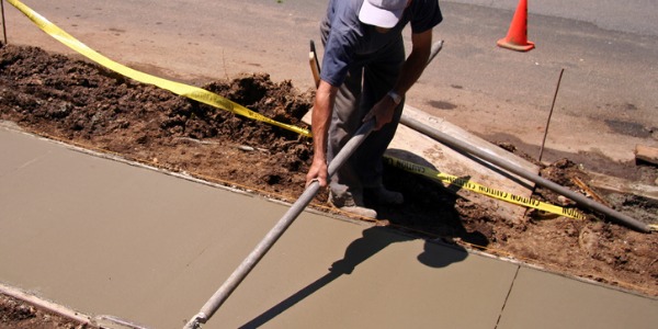 A cement mason smoothing out a sidewalk.