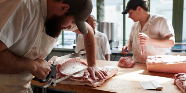 A butcher preparing a variety of cuts of meat, poultry, and fish for consumers to buy.