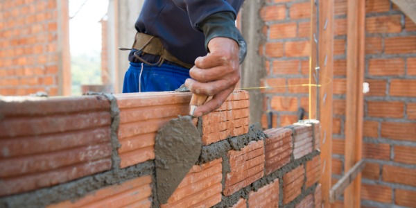 A brickmason using bricks to build a wall.