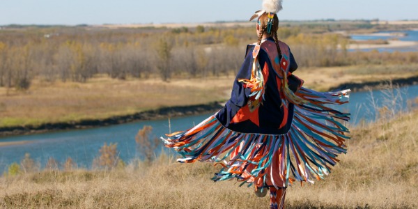 Native Indian woman dancing outside in the field wearing authentic clothing.