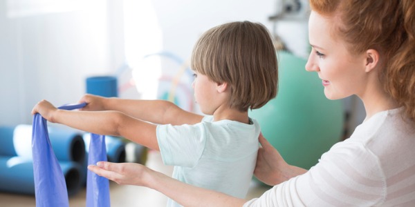 A physical therapist helping a child with his treatment by having him use an elastic exercise band.