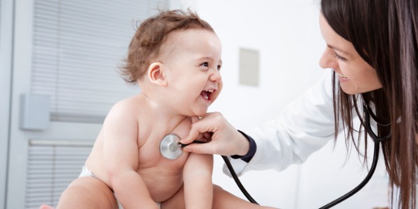 A pediatric cardiologist checking a laughing baby's heartbeat with a stethoscope.