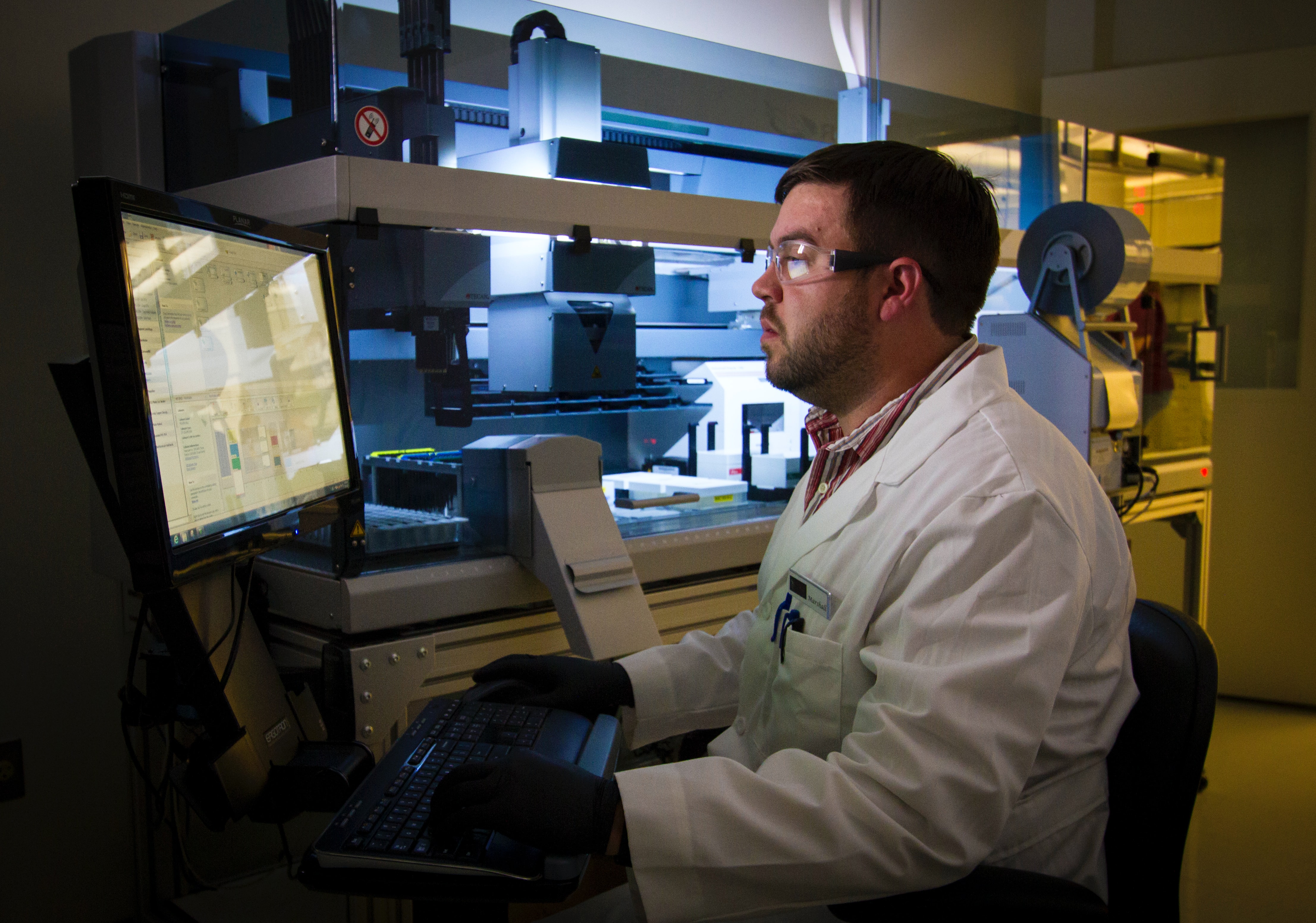 Un hombre con bata de laboratorio mira los datos en la pantalla de un ordenador.