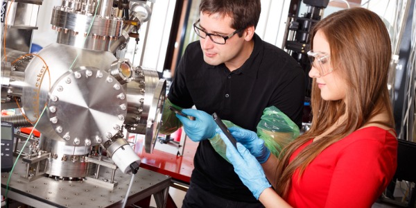 Two engineering physicists working with a laser deposition chamber.