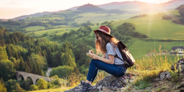 A travel writer sitting on top of a hill overlooking beautiful scenery, and jotting down notes.