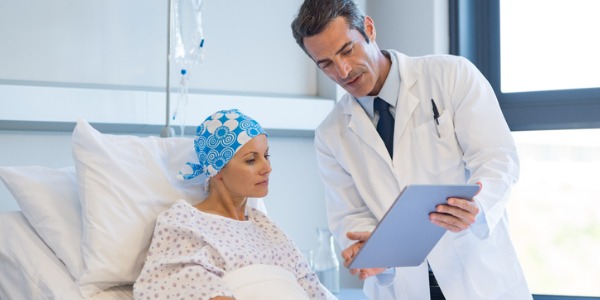 An oncologist speaking with his patient at her hospital bed.