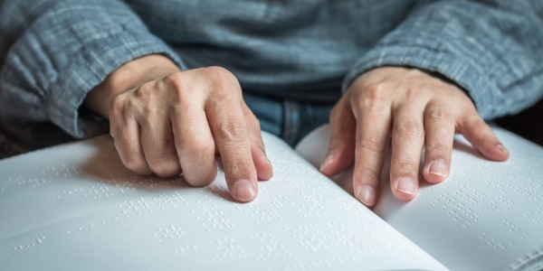 A person reading a book that has been transcribed into Braille by a Braille transcriber.