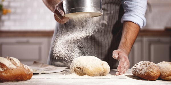 A baker sifting flour over bread dough.