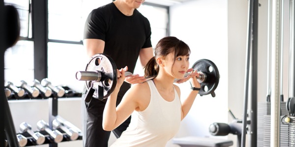 A personal trainer helping their client train with a barbell.